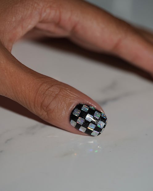 a thumb nail with black nail polish and a disco ball design with holographic squares