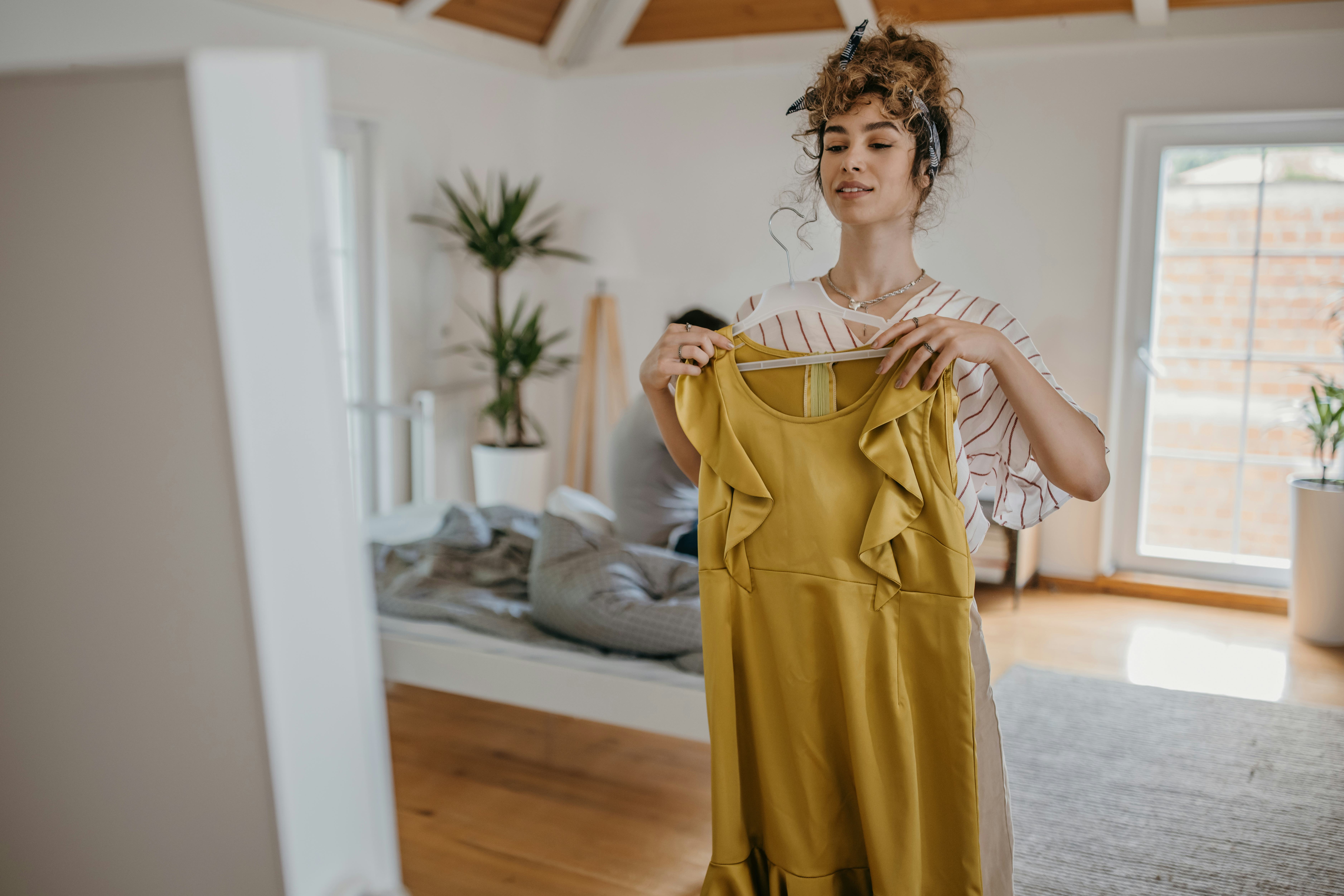Millennial woman looking at rental dress in a mirror at home.