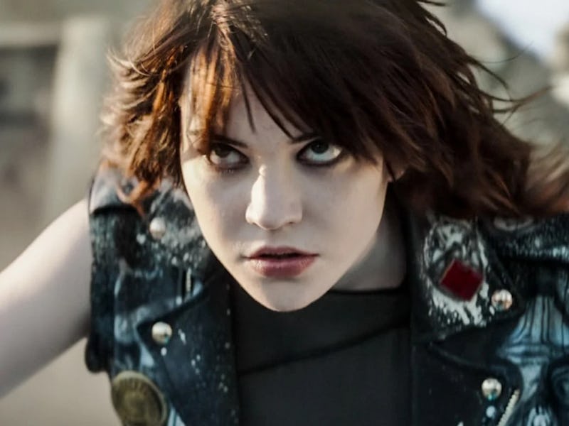 A young woman with striking features and intense expression, wearing a studded leather vest, stares ...