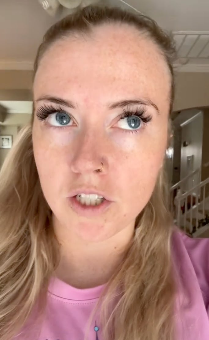 A close-up of a woman with blonde hair and bright blue eyes, wearing a pink shirt. She appears to be mid-sentence, expressing strong emotion.