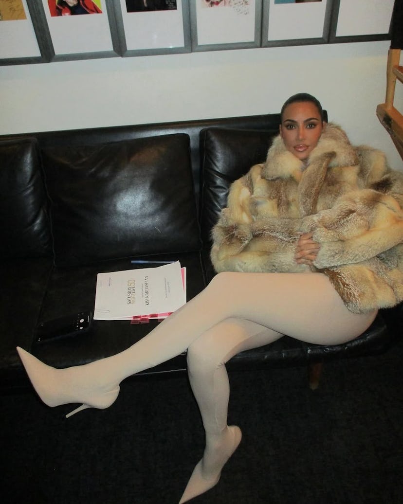Kim in a big fur coat sitting on a couch