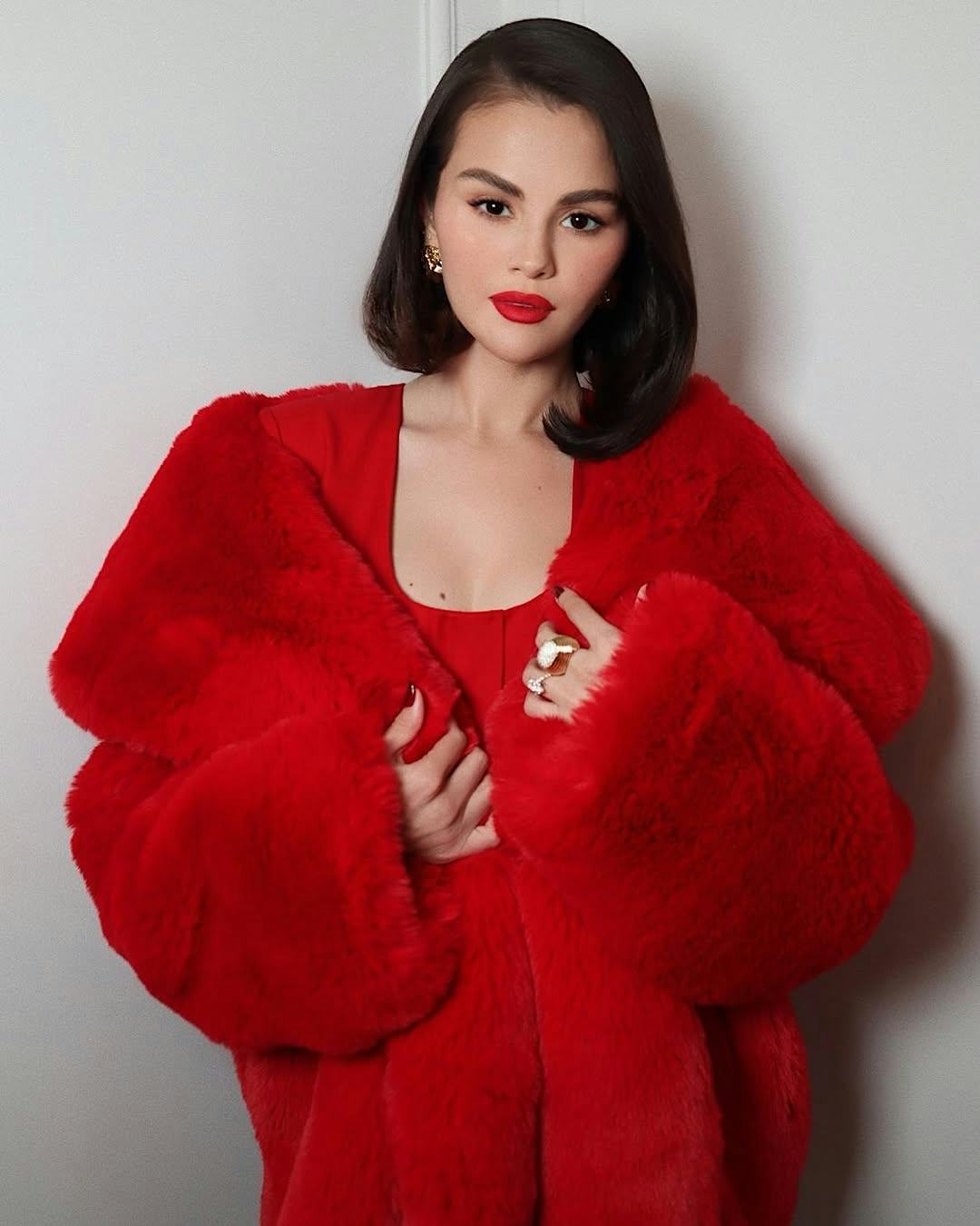 Selena Gomez wears a red fur coat and dress.