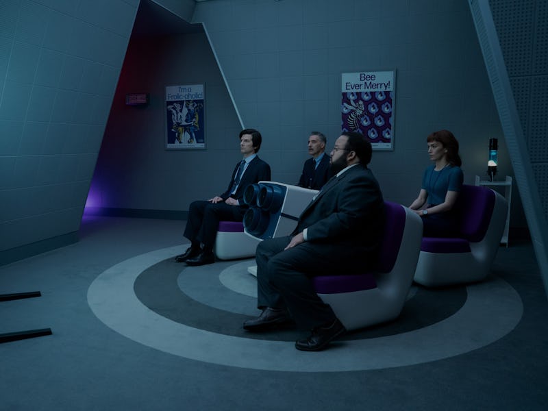 A group of four people sits in modern chairs, attentively watching a screen in a dimly lit, futurist...