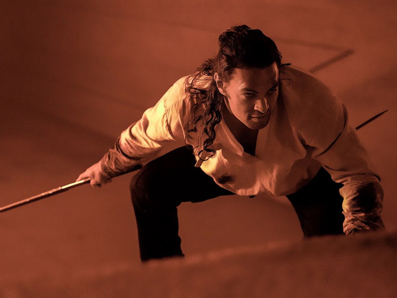 A man with long hair crouches in an action pose, holding a weapon. The scene is dimly lit with warm ...