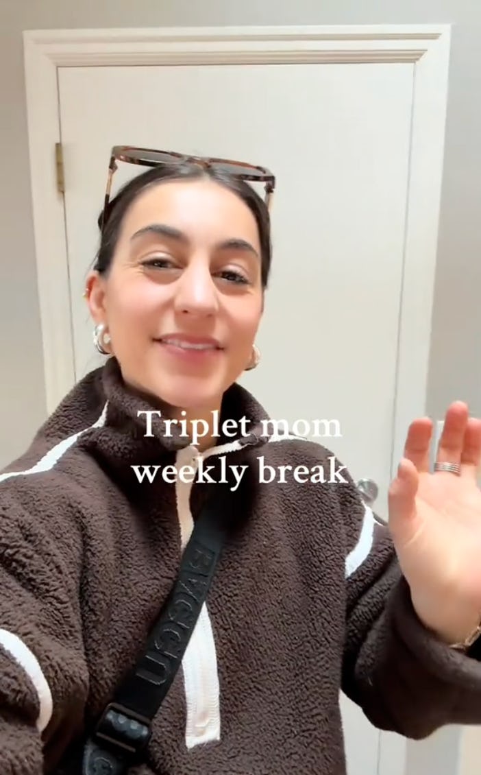 A smiling woman in a cozy brown jacket waves at the camera, with the text "Triplet mom weekly break" displayed above her. A simple interior is visible in the background.