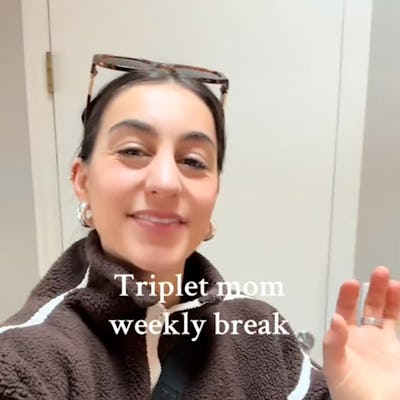 A smiling woman in a cozy brown jacket waves at the camera, with the text "Triplet mom weekly break" displayed above her. A simple interior is visible in the background.