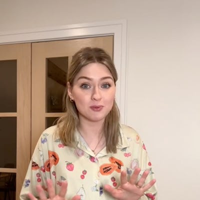 A young woman stands in front of a door, wearing colorful fruit-patterned pajamas. She gestures with her hands, expressing excitement or surprise.