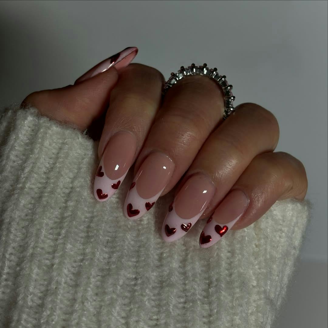 almond-shaped French tip nails with pink tips and red metallic hearts