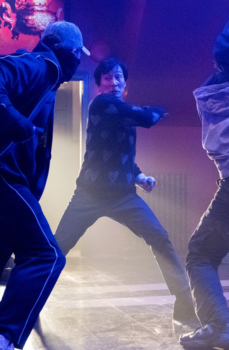 Three individuals engage in a dynamic fight scene in a colorful, dimly lit room, with dramatic light...