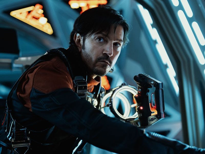 A man in a futuristic control room, wearing a black and red suit, intently engages with a console, i...