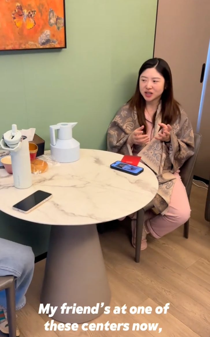 A woman sits at a table, wearing pajamas, in a postpartum hotel in China.