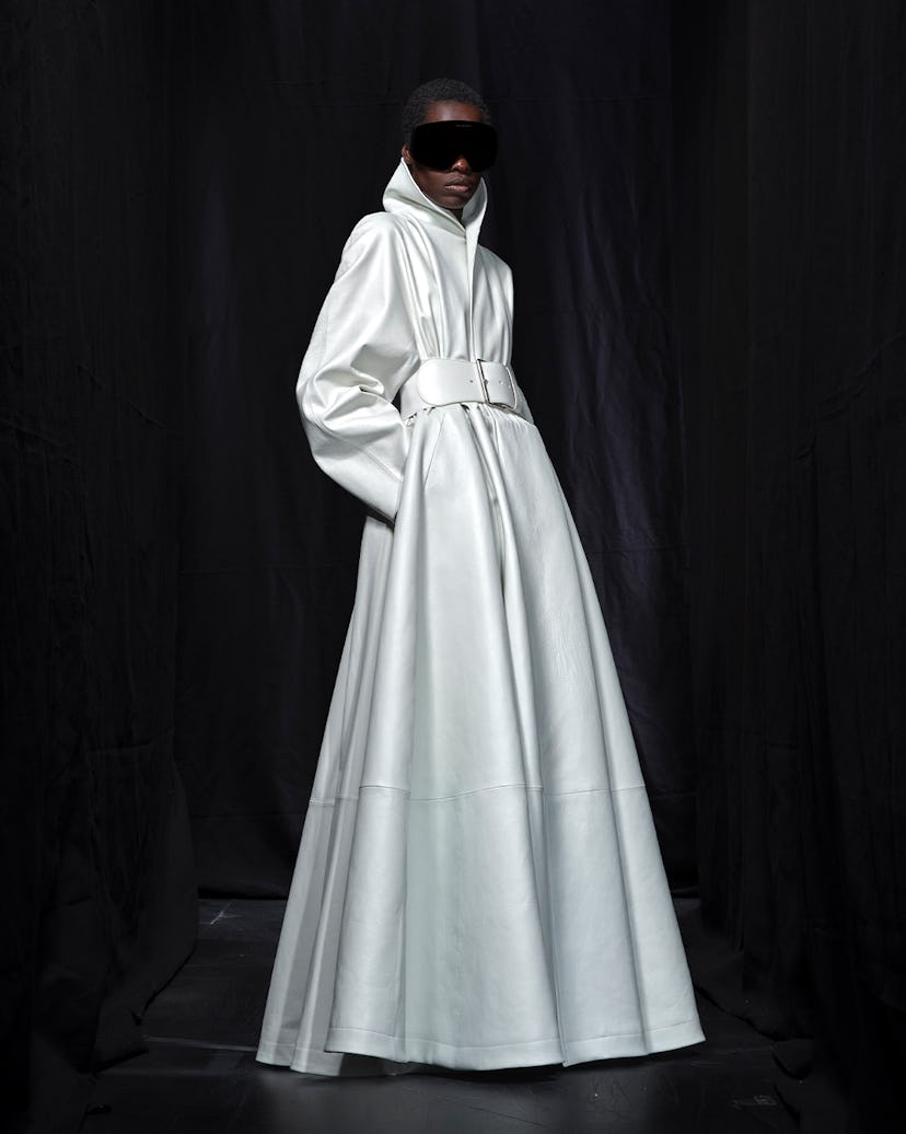 A model wearing black sunglasses and a white coat