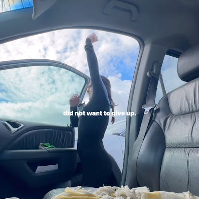A woman in a wet suit stretches in front of her car door.