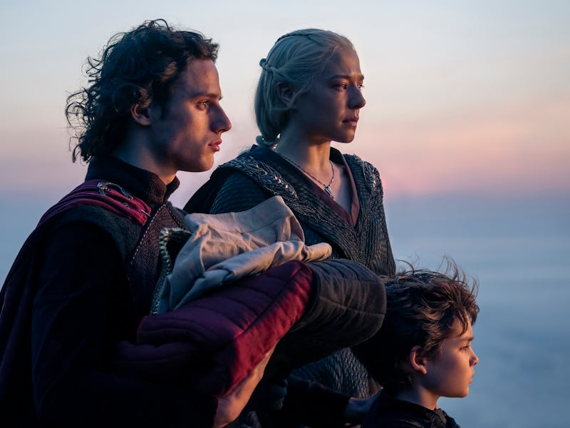 A man, a woman, and a child stand together against a serene sunset backdrop, gazing into the distanc...