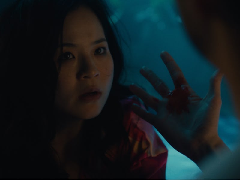 A woman with dark, wavy hair looks intently at another person, holding her hand up with blood on it ...