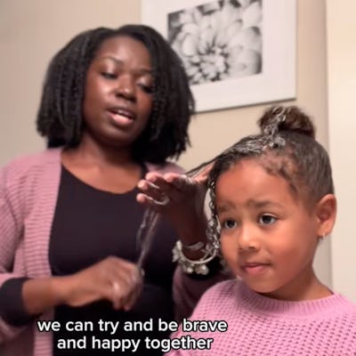 A woman styles a young girl's hair in a bathroom, both smiling. The girl wears a pink sweater and colorful bracelets, with text encouraging bravery and happiness together.