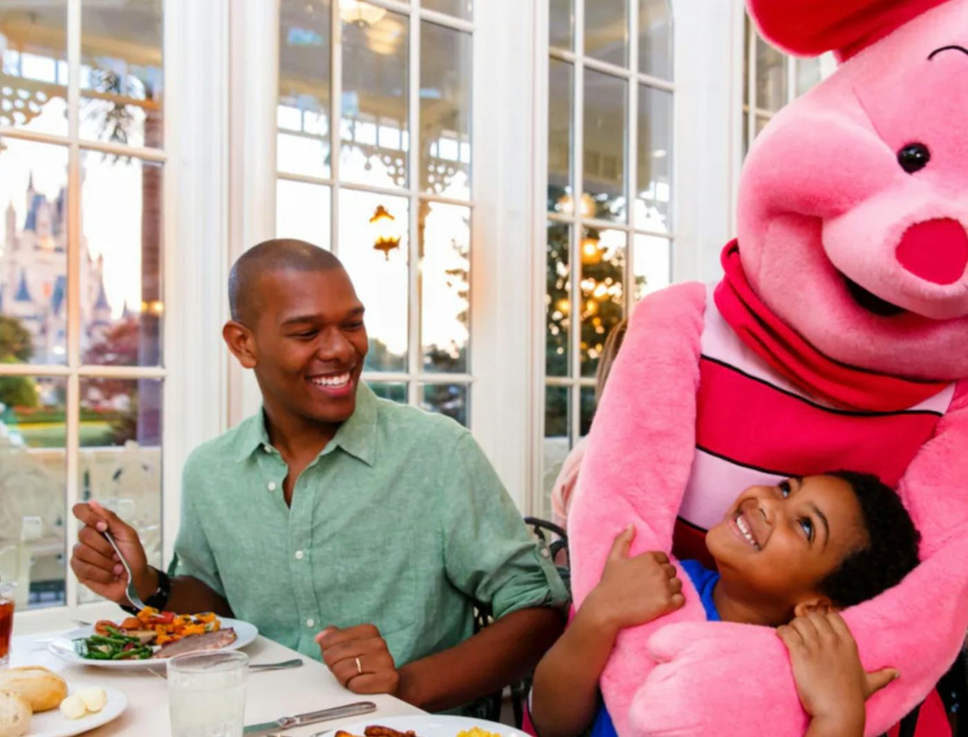 A joyful father and son share a meal with Piglet. They're seated near a window with a castle view.