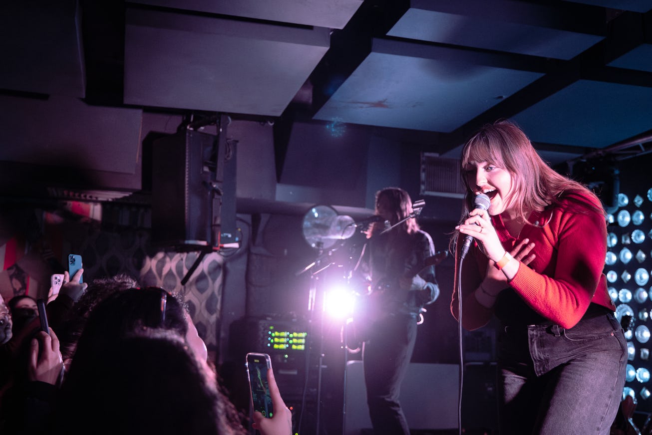 A vibrant live music scene featuring a female singer passionately performing into a microphone, whil...