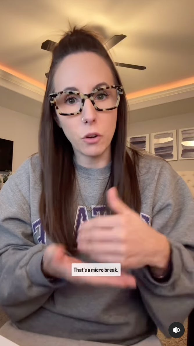 A woman with long brown hair, wearing a gray sweatshirt and stylish glasses, gestures as she talks about taking a "micro break."