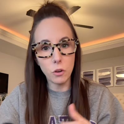 A woman with long brown hair, wearing a gray sweatshirt and stylish glasses, gestures as she talks about taking a "micro break."