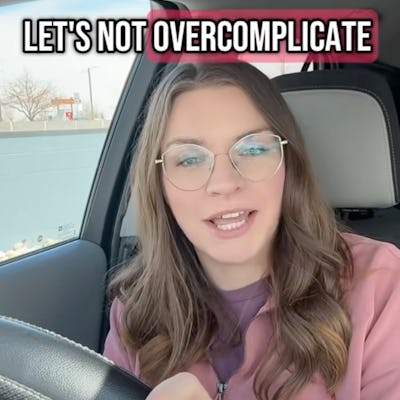 A young woman with long brown hair and glasses sits in a car, smiling and speaking to the camera. Text above her reads "LET'S NOT OVERCOMPLICATE."