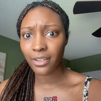 A young woman with braided hair looks surprised and questioning. She is indoors with a green wall backdrop, wearing a sleeveless floral top.