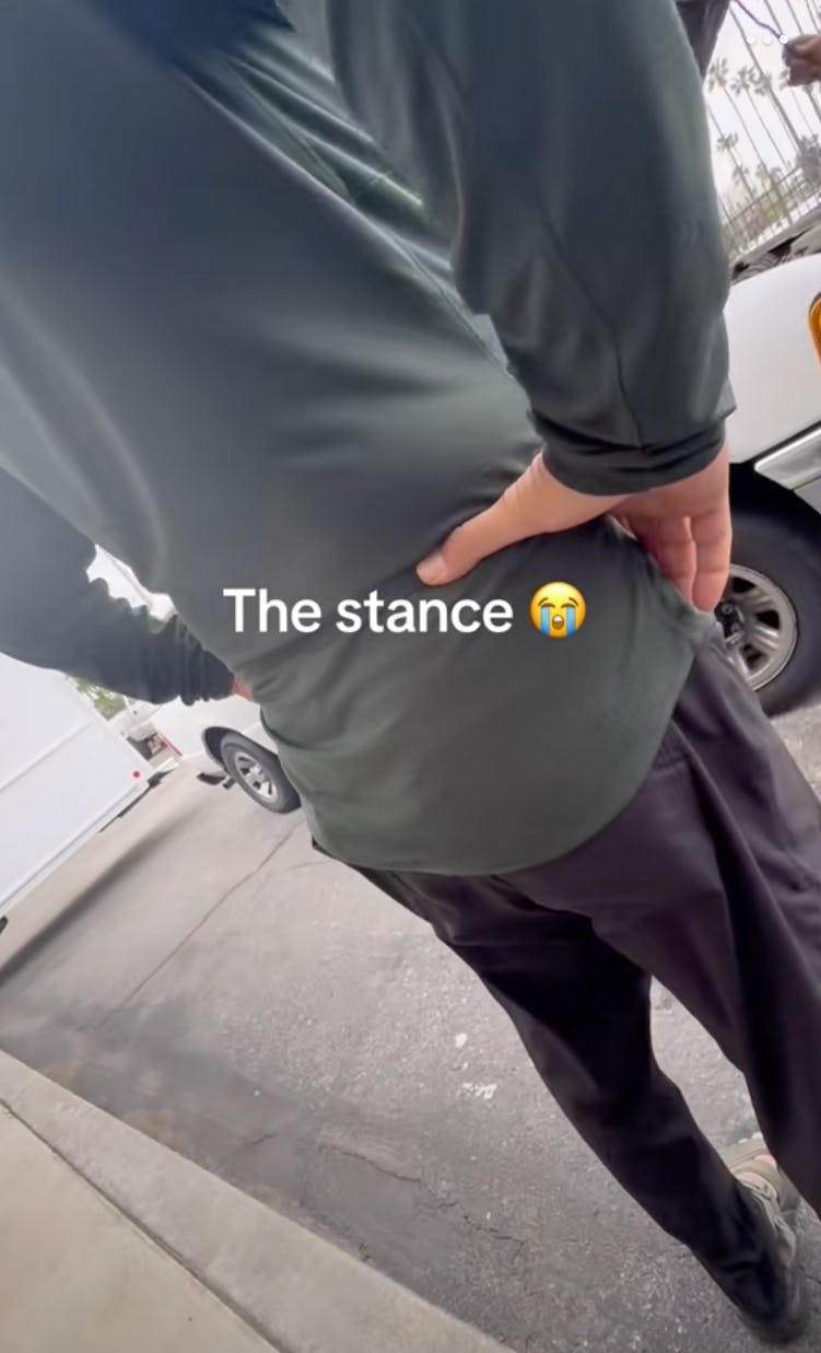A person stands with their back to the camera, wearing a long-sleeve green shirt and dark pants. Text overlay reads "The stance 😢."