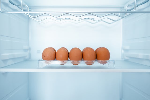 A clear refrigerator shelf holds a row of five brown eggs in a tray, surrounded by a bright, cool in...