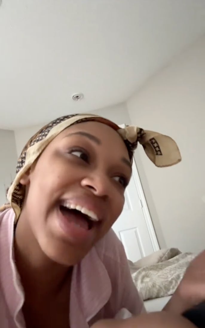 A woman with a headscarf smiles and talks animatedly while lounging in bed, surrounded by soft pillo...