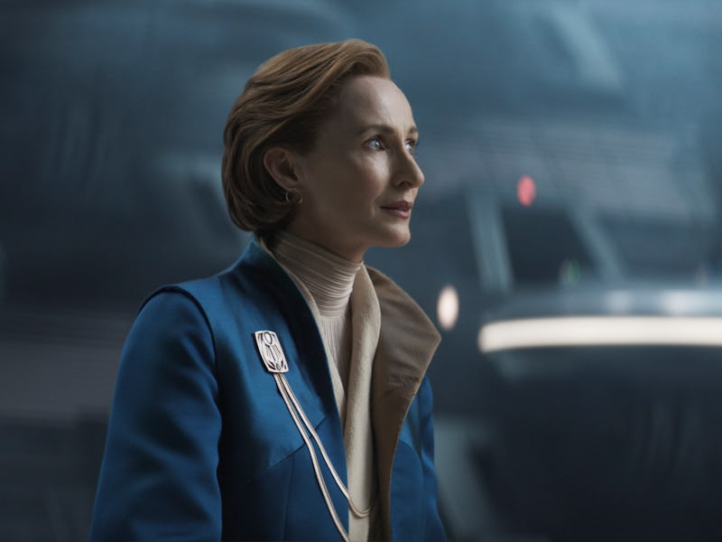 A woman in a blue uniform stands confidently in a futuristic space setting, with sleek, illuminated ...