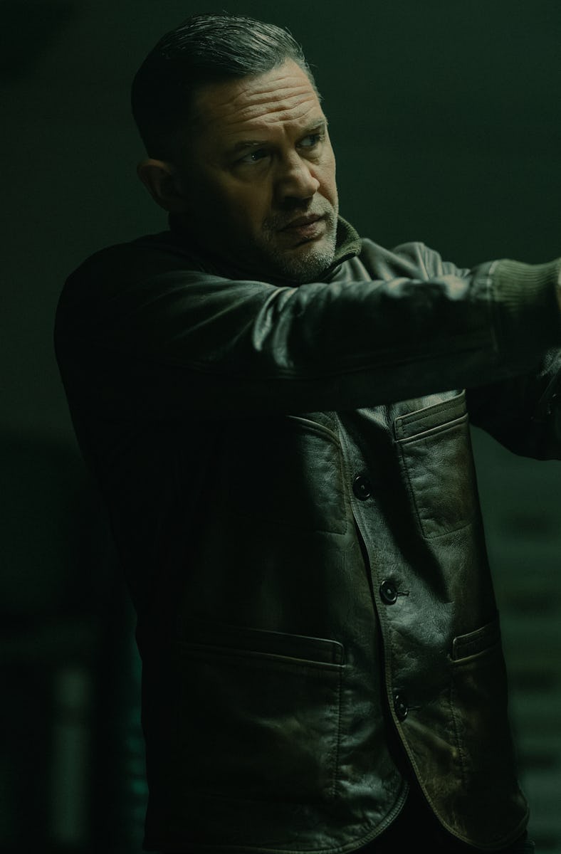 A man in a dark leather jacket aims a handgun in a dimly lit setting, exuding a tense and focused de...