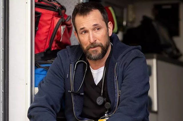 Noah Wyle playing Dr. Robby in The Pitt, sitting in the back of an ambulance smirking.