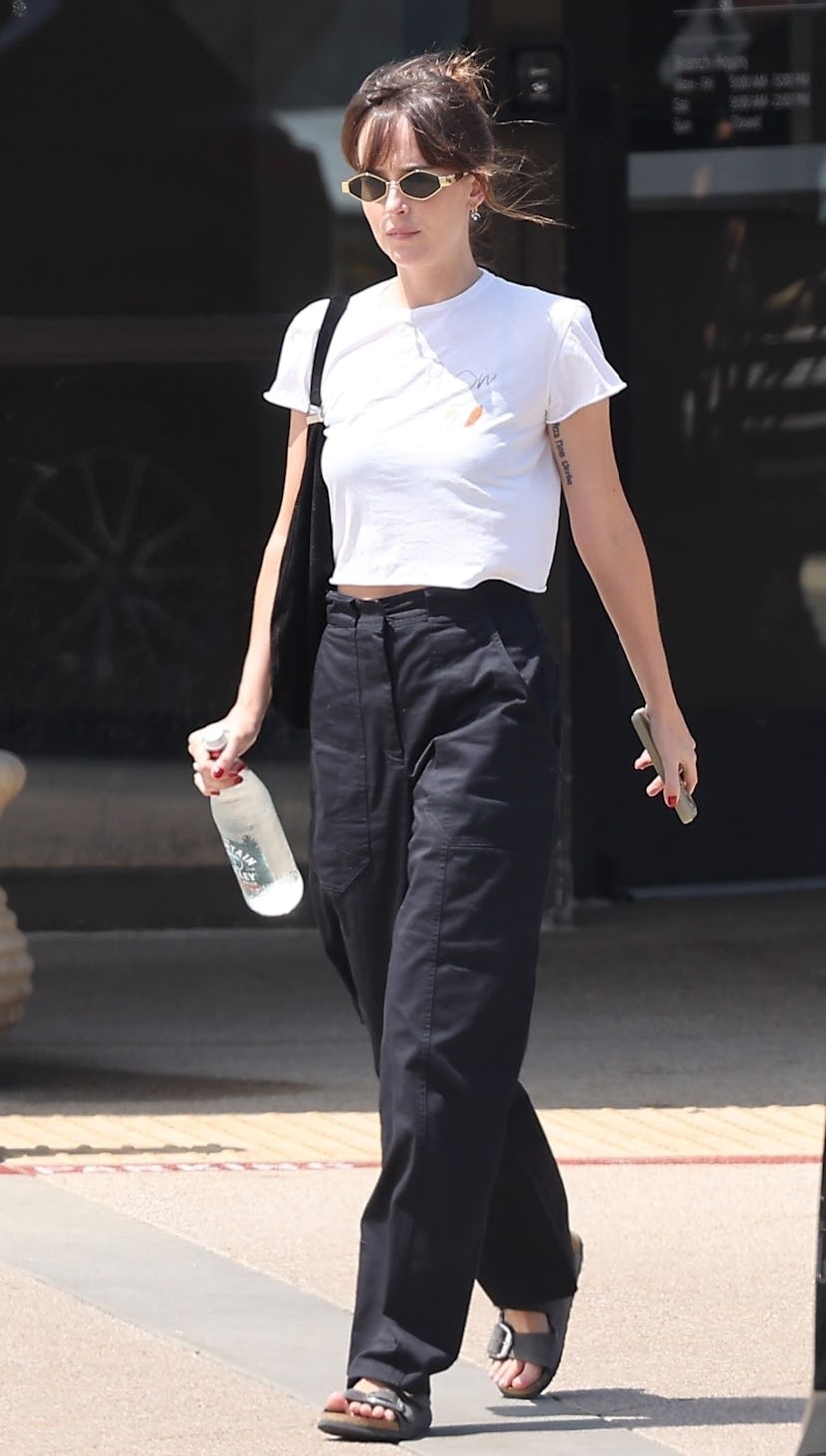 Dakota Johnson wears a white tee, black trousers, and Birkenstocks.