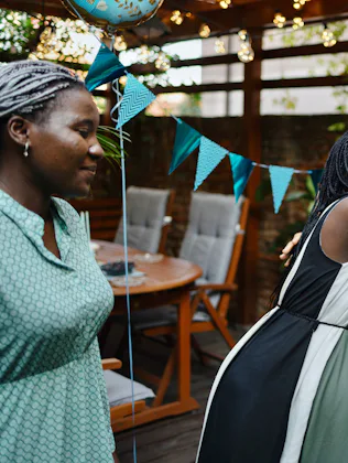 A joyful gathering of women celebrating, with one woman embracing another. The outdoor space is deco...