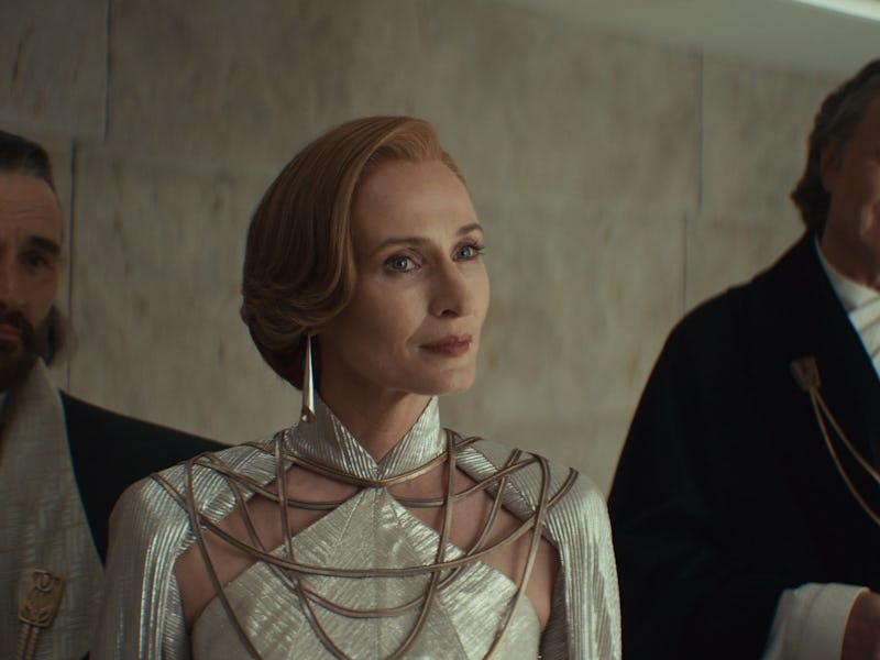 A group of three characters in elegant attire stands in a modern, minimalistic setting. The woman in...
