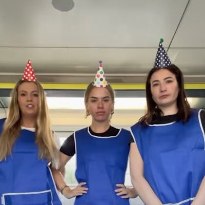 Three women in blue aprons and party hats stand together, smiling playfully. Text below reads about a friend feeling stressed after having a baby.