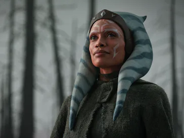 A character with blue and white striped head-tails, wearing a dark cloak, stands confidently against...