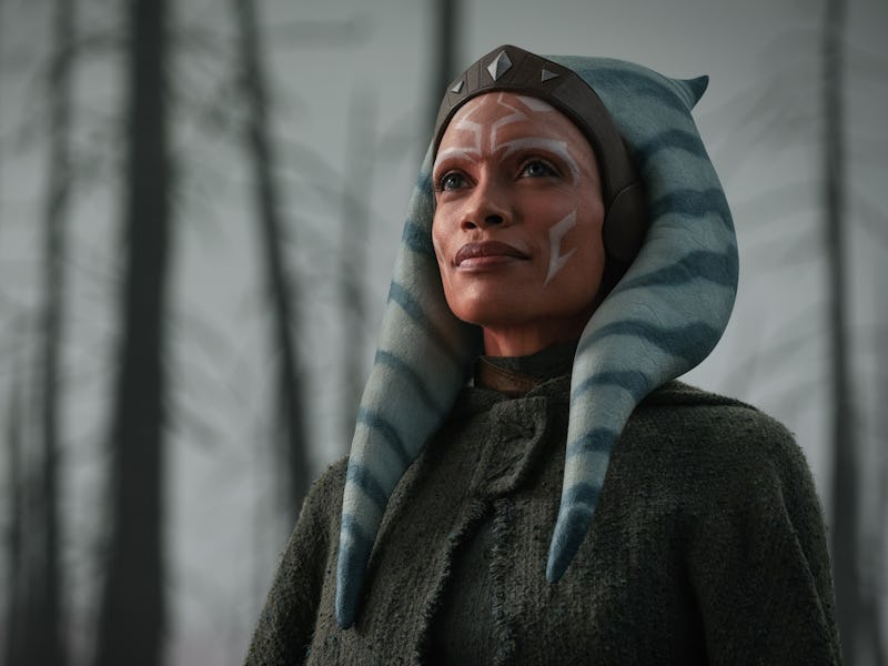 A character with blue and white striped head-tails, wearing a dark cloak, stands confidently against...