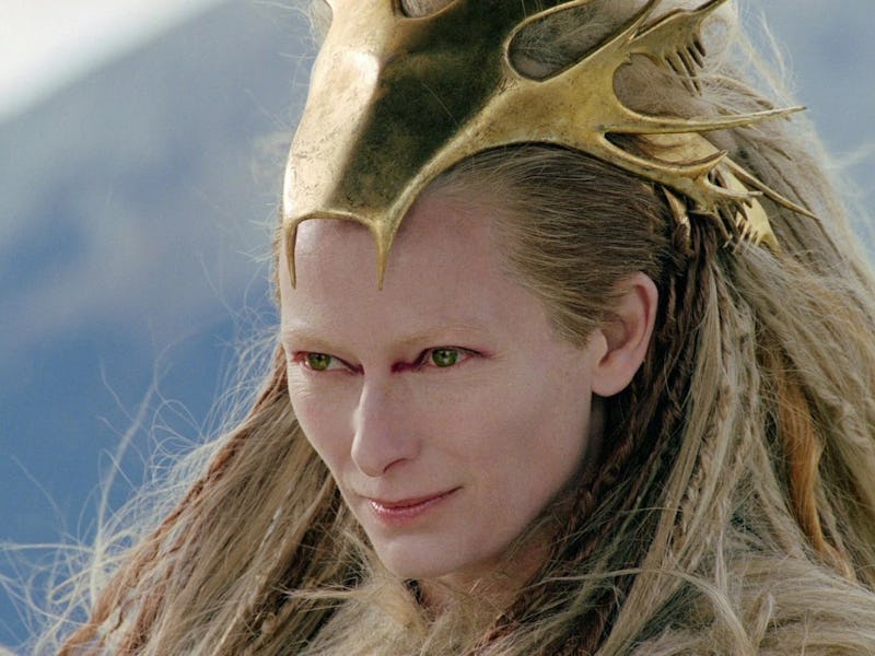 A person with long, flowing hair adorned with a striking gold crown features intense gaze and pale s...