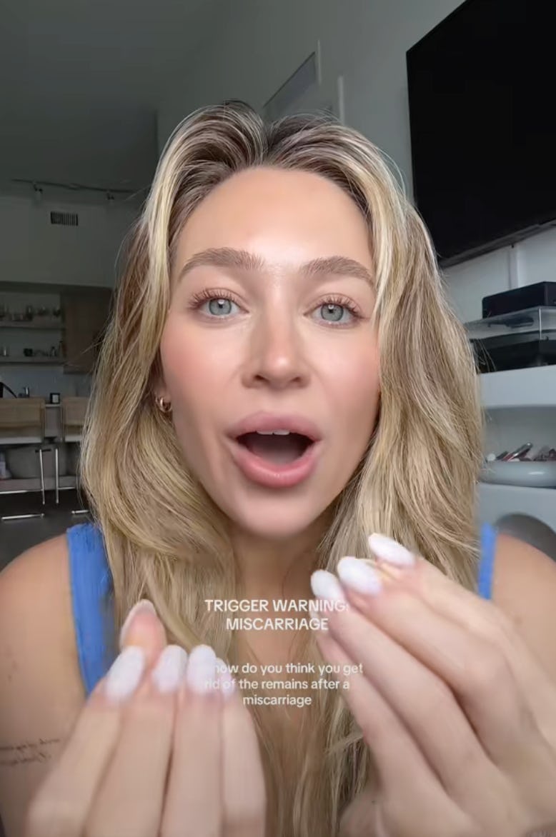 A young woman with long blonde hair and light makeup speaks towards the camera, gesturing with her h...