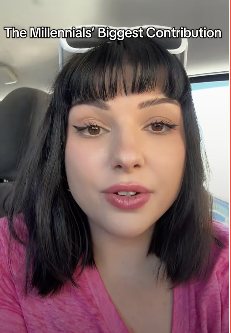 A young woman with shoulder-length black hair and full lips speaks directly to the camera, wearing a pink top. The background appears to be a vehicle interior.