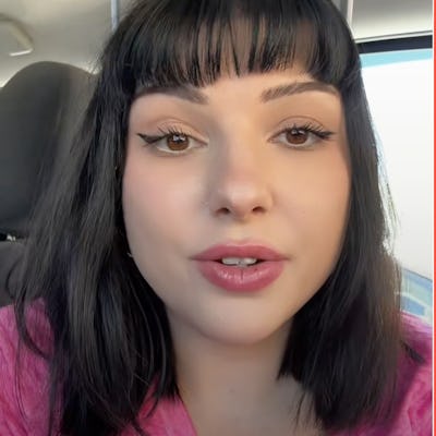 A young woman with shoulder-length black hair and full lips speaks directly to the camera, wearing a pink top. The background appears to be a vehicle interior.