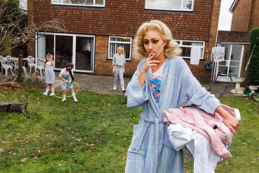 nadia lee cohen dressed up in a blonde wig in a backyard holding a laundry basket and smoking a ciga...