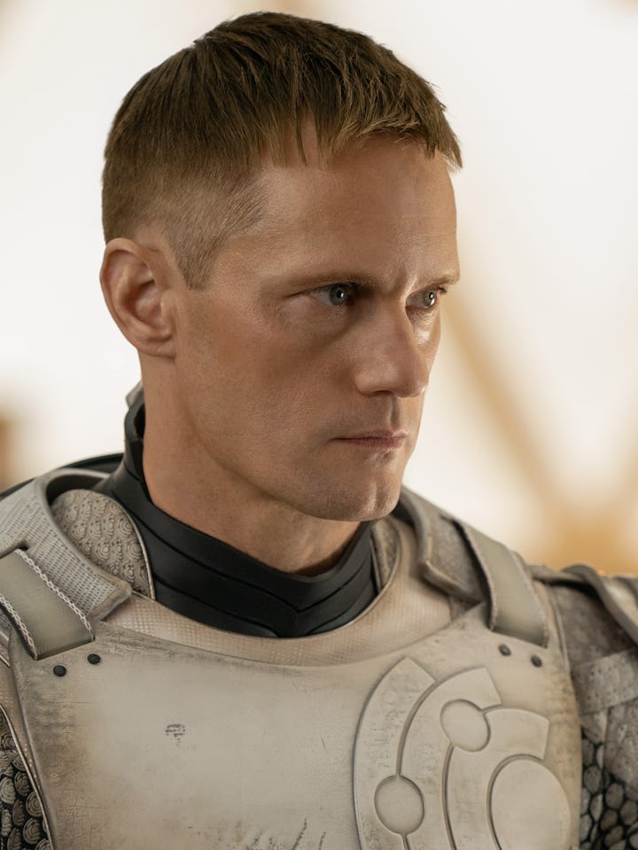 A close-up of a man in futuristic armor, with short blond hair and a serious expression. The backgro...