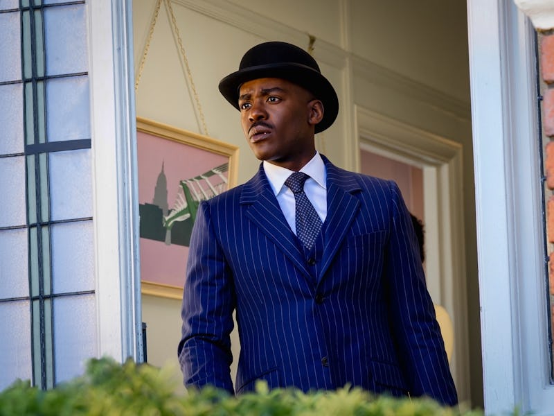 A man in a pinstripe suit and black hat stands at an open window, gazing outside thoughtfully. The i...