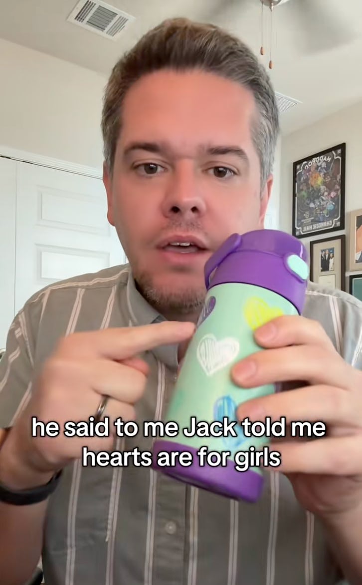 A person with short hair and a goatee holds a colorful water bottle while speaking, with text overlay discussing a comment about hearts being for girls.