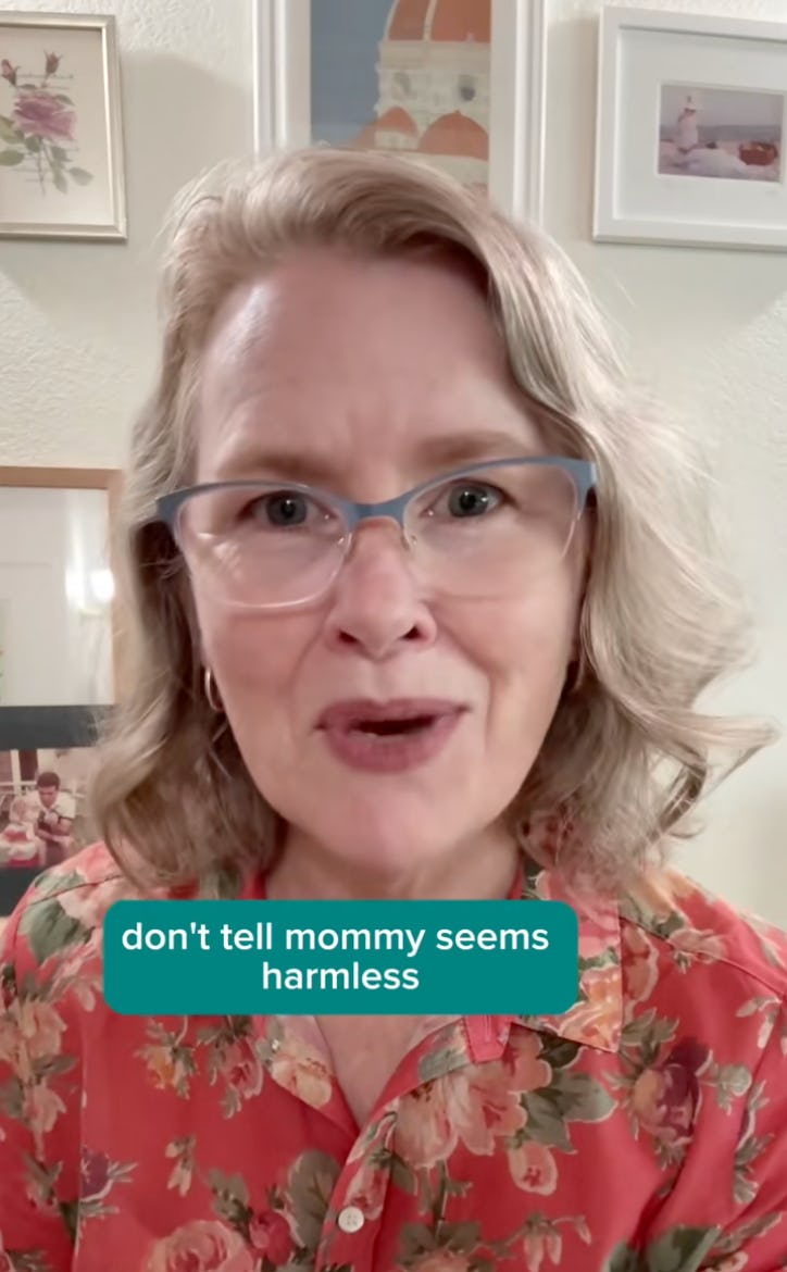 A woman with short, wavy hair and glasses smiles at the camera. She wears a floral shirt. Text overlay reads: "don't tell mommy seems harmless." Background features light-colored walls with framed pictures.