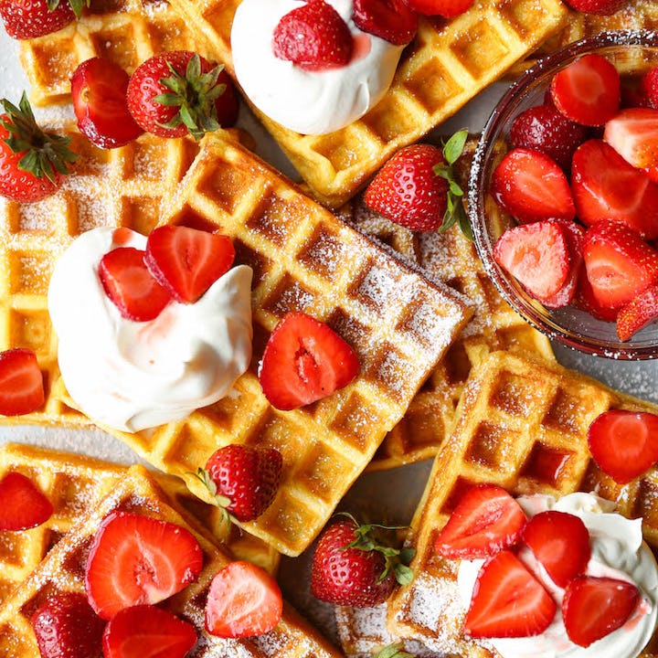 Waffles with strawberries and cream on top, in a story about mother's day breakfast and brunch recip...