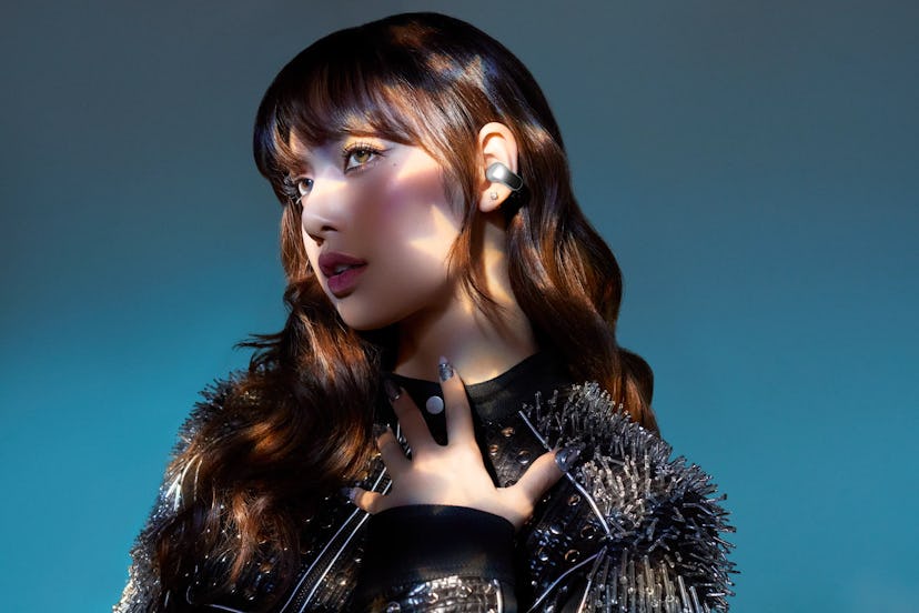 A young woman poses in profile against a gradient backdrop, wearing stylish earbuds and a striking o...