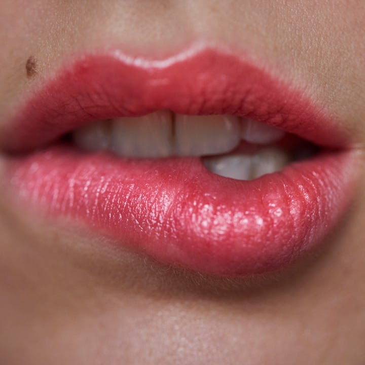 Close-up of a pair of full, gently parted lips, enhanced with glossy pink lipstick. A small mole is ...